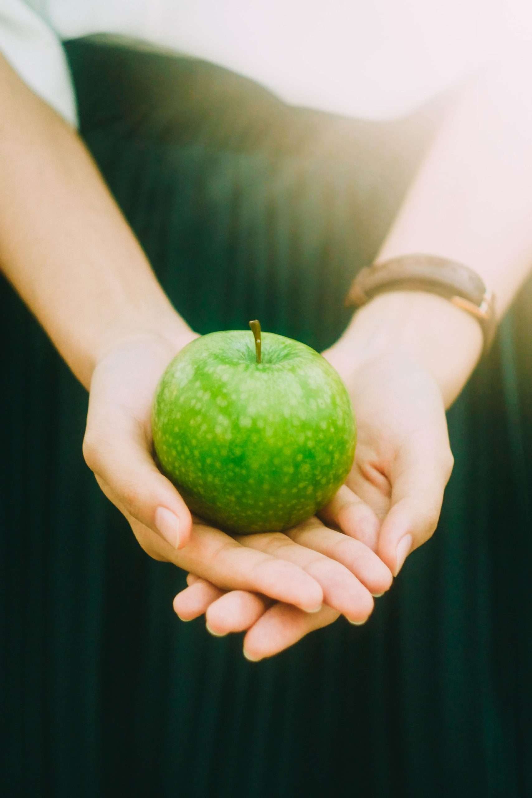 zwei Hände halten einen grünen Apfel